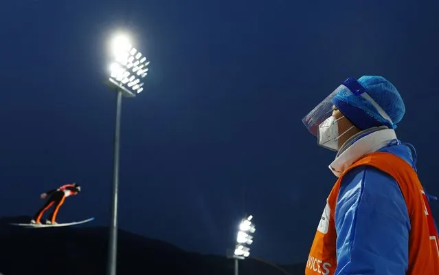 A member of the medical crew watches Andrei Feldorean of Romania in action during men's ski jumping at the 2022 Beijing Olympics, at the National Ski Jumping Centre in Zhangjiakou, China on February 11, 2022. (Photo by Kai Pfaffenbach/Reuters)