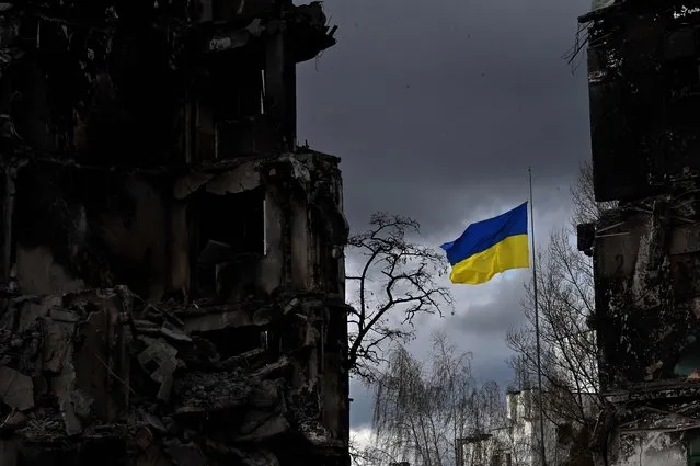 The Ukrainian flag flutter between buildings destroyed in bombardment, in the Ukrainian town of Borodianka, in the Kyiv region on April 17, 2022. Russia invaded Ukraine on February 24, 2022. (Photo by Sergei Supinsky/AFP Photo)