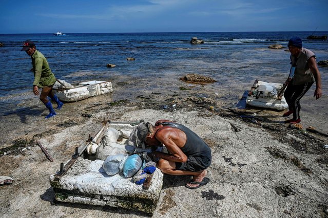 A group of Cuban fishermen drag their makeshift rafts after fishing in Havana Bay on July 22, 2024. When the weather permits, artisanal fishermen take to the water in improvised polystyrene rafts to make up for the lack of means and fuel. (Photo by Yamil Lage/AFP Photo)