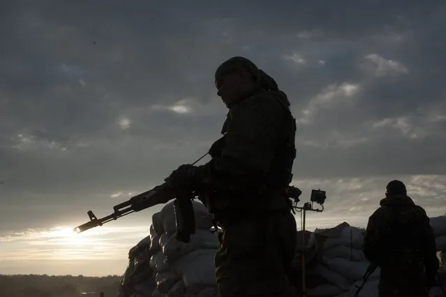 Pro-Russian fighters stand guard at a check point in the village of Karlivka near Donetsk, eastern Ukraine, Wednesday, June 18, 2014, during a handover of the bodies of Ukrainian troops who died in a plane shot down near Luhansk. The two sides managed to arrange a brief truce Wednesday evening in the eastern town of Karlivka to allow pro-Russian forces to hand over the bodies of 49 Ukrainian troops who died when the separatists shot down a transport plane bound for the airport in Luhansk last weekend. (Photo by Evgeniy Maloletka/AP Photo)