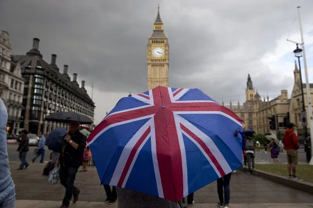 A pedestrian shelters from the rain beneath a Union flag themed umbrella as they walk near the Big Ben clock face and the Elizabeth Tower at the Houses of Parliament in central London on June 25, 2016, following the pro-Brexit result of the UK's EU referendum vote. The result of Britain's June 23 referendum vote to leave the European Union (EU) has pitted parents against children, cities against rural areas, north against south and university graduates against those with fewer qualifications. London, Scotland and Northern Ireland voted to remain in the EU but Wales and large swathes of England, particularly former industrial hubs in the north with many disaffected workers, backed a Brexit. (Photo by Justin Tallis/AFP Photo)