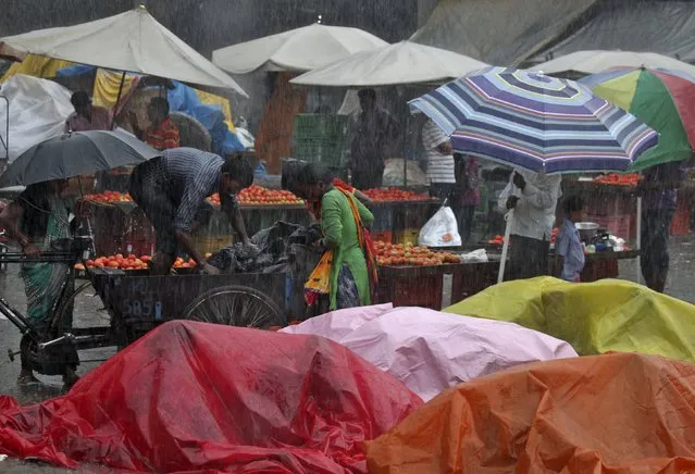 Vendors take shelter under plastic tarpaulins as others work during a heavy rain shower at a wholesale vegetable market in Chandigarh, India, August 11, 2015. India has received 6 percent lower rainfall than usual, but in some areas rainfall deficit is as high as 57 percent, India Meteorological Department (IMD) data showed. (Photo by Ajay Verma/Reuters)