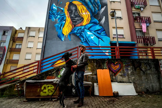 Portuguese artist Acer poses with his dog in front of his mural in Quinta do Mocho neighbourhood in Sacavem, outskirts of Lisbon, on November 11, 2019. (Photo by Patricia De Melo Moreira/AFP Photo)