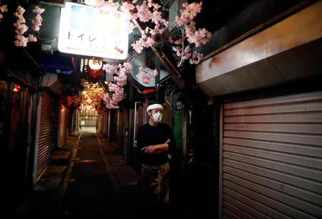 A staff member of a restaurant wearing a protective face mask stands at almost empty and temporary closed Japanese drinking bars' alley after the government announced the state of emergency for the capital following an outbreak of the coronavirus disease (COVID-19) at Shinjuku district in Tokyo, Japan April 8, 2020. (Photo by Issei Kato/Reuters)