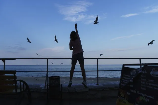 A woman feeds the birds along the Black Sea in Odesa, Ukraine, Friday, July 29, 2022. (Photo by David Goldman/AP Photo)