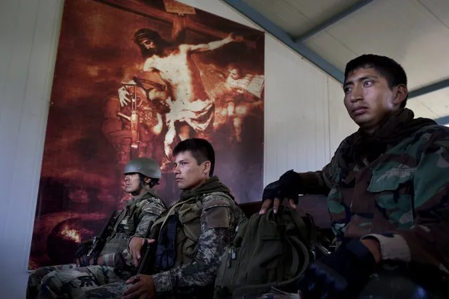 In this September 19, 2014 photo, soldiers sit, back dropped by an image of Jesus Christ embracing a praying soldier, inside a building at the Mazamari counternarcotics base in the Valley of the Ene and Apurimac and Mantaro River Valleys, or VRAEM, the world's No. 1 coca-growing region, in Junin, Peru. An average of about  4-5 small planes daily fly into Peru from Bolivia, picking up about 300 kilos each of coca paste worth about a third of a million dollars in Bolivia. (Photo by Rodrigo Abd/AP Photo)