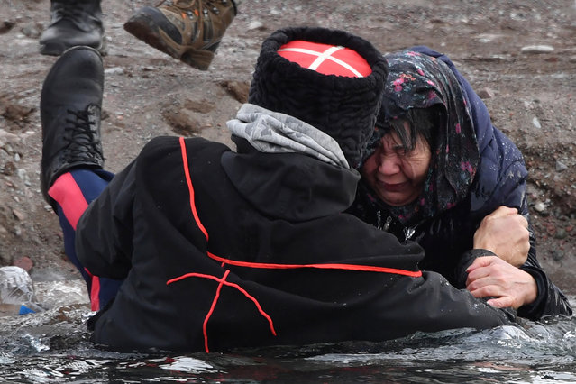 A cossack helps a woman get out of the Kara-Balta river during the celebration of the Epiphany holiday near the village of Sosnovka, some 90 kms from Bishkek, on January 19, 2024. Among Orthodox Christians, the feast of Epiphany celebrates the day the spirit of God descended upon believers in the shape of a dove during Jesus Christ's baptism in the river Jordan. (Photo by Vyacheslav Oseledko/AFP Photo)