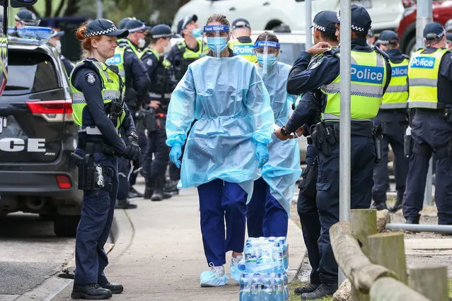 Medical staff wearing PPE holding material about to walk into the Flemington Public housing flats on July 05, 2020 in Melbourne, Australia. Nine public housing estates have been placed into mandatory lockdown and two additional suburbs are under stay-at-home orders as authorities work to stop further COVID-19 outbreaks in Melbourne. The public housing towers will be in total lockdown for at least five days following a high number of positive coronavirus cases recorded in residents on those estates. The towers will be closed and contained, and the only people allowed in and out will be those providing essential services. Police will be placed on each floor of the towers and other police will control access points to the estates. Residents of 12 Melbourne hotspot postcodes are also on stay-at-home orders and are only able to leave home for exercise or work, to buy essential items including food or to access childcare and healthcare. Businesses and facilities in these lockdown areas are also restricted and cafes and restaurants can only open for takeaway and delivery. (Photo by Asanka Ratnayake/Getty Images)