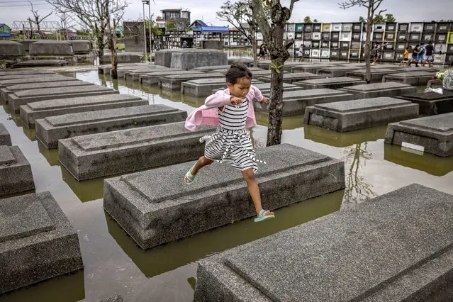 A girl jumps across tombs at a flooded cemetery following Tropical Storm Nalgae, as Filipinos mark All Saints' Day on November 01, 2022 in Masantol, Pampanga province, Philippines. Millions of Filipinos flock to cemeteries around the country to visit departed loved ones on All Saints' Day, a holiday celebrated in Latin cultures around the world during which family and friends of the deceased gather at cemeteries to pray and hold vigils for those who have passed away. (Photo by Ezra Acayan/Getty Images)