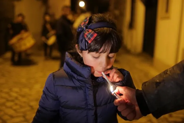 An adult helps a young girl light a cigarette as a band plays in the background in the village of Vale de Salgueiro, northern Portugal, during the local Kings' Feast Friday, January 5, 2018. (Photo by Armando Franca/AP Photo)