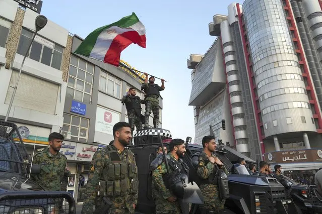 An anti-riot police officer waves a representation of the Iranian flag during a street celebration after Iran's national soccer team defeated Wales in Qatar's World Cup, at Sadeghieh Sq. in Tehran, Iran, Friday, November 25, 2022. Iran's political turmoil has cast a shadow over Iran's matches at the World Cup, spurring tension between those who back the team and those who accuse players of not doing enough to support the protests that started Sept. 16 over the death of a 22-year-old woman in the custody of the morality police. (Photo by Vahid Salemi/AP Photo)