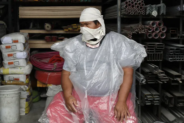 A worker wears an improvised mask to curb the spread of COVID19 and plastic sheet to protect him from rain at the border of the Bulacan province and Caloocan city, Philippines, as they undergo stricter quarantine measures on Monday August 10, 2020. The capital and outlying provinces recently returned to another lockdown after medical groups warned that the country was waging a losing battle against the coronavirus amid an alarming surge in infections. (Photo by Aaron Favila/AP Photo)