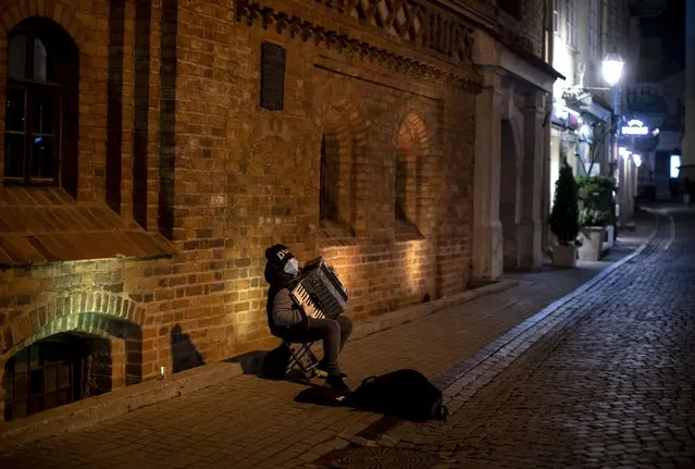 Pavel, a young street musician, wears a face mask to prevent the spread of coronavirus as he plays his accordion in an empty Old Town in Vilnius, Lithuania, Friday, October 30, 2020. Given the deteriorating epidemiological situation in the country, the Government has taken a decision in its Wednesday sitting to impose restrictions on events and gatherings organised in public places from 30 October to 13 November 2020. (Photo by Mindaugas Kulbis/AP Photo)