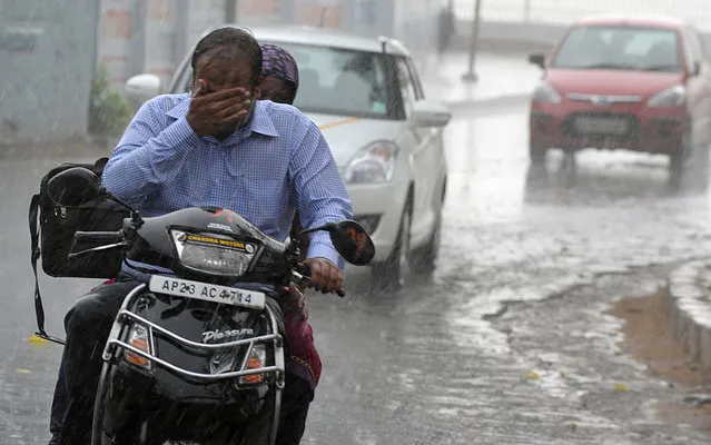 An Indian commuter wipes his face as he rides his scooter during unexpected rain in Hyderabad during World Earth Day on April 22, 2013. India's monsoon, vital to hundreds of millions of farmers and of crucial importance to the economy, will likely be normal this year, a report said earlier this month. (Photo by Noah Seelam/AFP Photo)