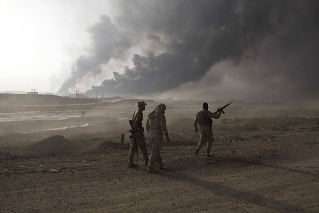Iraqi army soldiers man a checkpoint as oil wells burn on the outskirts of Qayyarah, Iraq, Wednesday, October 19, 2016. A senior Iraqi general on Wednesday called on Iraqis fighting for the Islamic State group in Mosul to surrender as a wide-scale operation to retake the militant-held city entered its third day. (Photo by Marko Drobnjakovic/AP Photo)