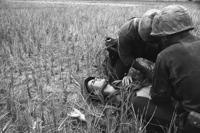 Pain etches the face of U.S. Marine as he gets his wound bandaged by medical corpsman Frank Saddler, background, and Cpl. Marvin Shirley, after being hit in the stomach by Viet Cong sniper fire at Le My, South Vietnam, May 4, 1965. Saddler later took the wounded leatherneck's rifle and ran off saying, “I may be needed some place else”. (Photo by Eddie Adams/AP Photo)