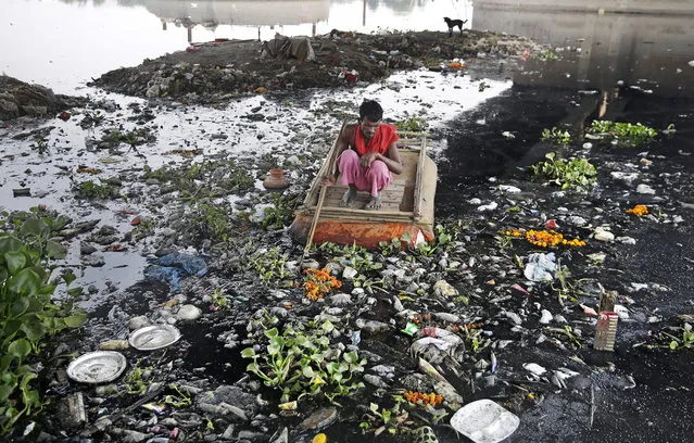 In this photo taken May 28, 2018, Ram Nath, 40, who makes a living from recycling trash, rummages for plastic bottles and other reusable trash while rowing a makeshift boat through murky waters of Yamuna, India's sacred river that flows through the capital of New Delhi. India produces more than 68 million tons of trash every day. More than 17,000 tons of it is plastic. That requires immense dumps, which in cities like New Delhi, mean hills of stinking trash up to 50 meters tall. Last year, two people were killed when a large part of one of the city’s dumps crashed down onto them. (Photo by Altaf Qadri/AP Photo)