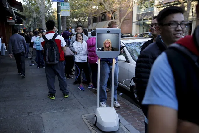 Brianna Lempesis, from San Diego, appears on a video screen on her “Beam” robot, while waiting in line to purchase an iPhone 6S at the Apple store in Palo Alto, California September 25, 2015. Lempesis made the purchase via the screen and the phone was attached to a hook on the robot. (Photo by Robert Galbraith/Reuters)