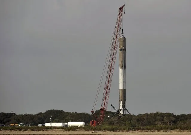 A crane steadies the SpaceX Falcon 9 booster rocket as it rests on a landing zone near the Atlantic Ocean in Cape Canaveral, Florida, December 22, 2015. The rocket blasted off with a payload of communications satellites before the reusable main-stage booster turned around, soared back to Cape Canaveral and landed safely. (Photo by Steve Nesius/Reuters)