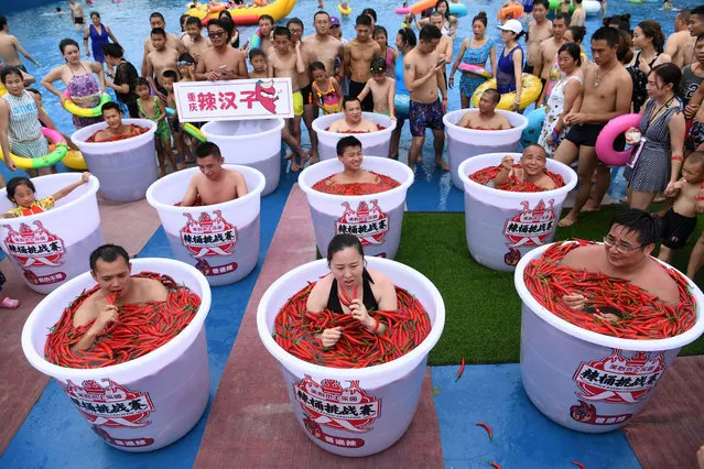 Participants take a bath in barrels filled with chilli peppers during the Spicy Barrel Challenge contest inside a water park in Chongqing, China July 7, 2018. (Photo by Chen Chao/CNS via Reuters)