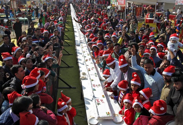 People pose next to a 251-feet-long (76-metres) cake during Christmas celebrations at a consumer fair in Chandigarh, India, December 25, 2015. (Photo by Ajay Verma/Reuters)