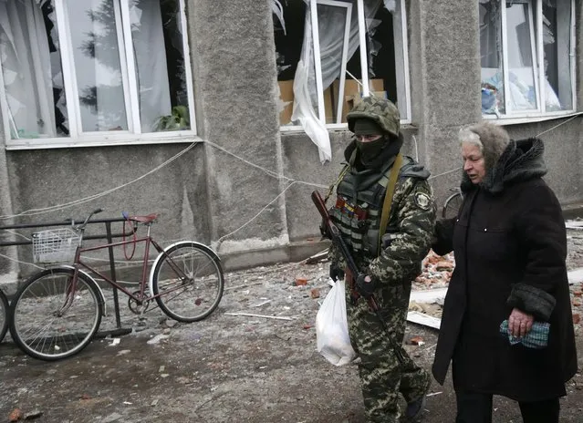 Soldier helps an elderly woman to carry a bag of supplies outside of the humanitarian aid distribution center in the town of Debaltseve, Ukraine, Friday, February 6, 2015. (Photo by Petr David Josek/AP Photo)
