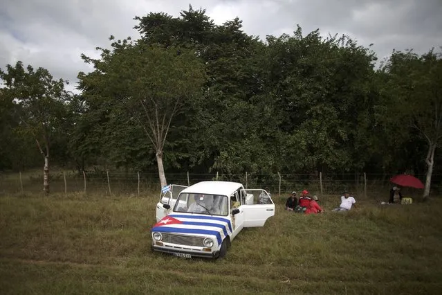 People display a Cuban flag atop a car as they await the arrival of the caravan carrying the late Cuban President's ashes in El Maja, Cuba, December 1, 2016. (Photo by Alexandre Meneghini/Reuters)