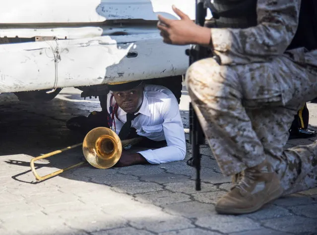 A member of the National Palace's music band shelters under a truck as a riot breaks out during the commemoration of the 212 anniversary of the murder of Jean Jacques Dessalins, in Port-au-Prince, Haiti, 17 October 2018. Several individuals threw stones during a commemoration event of the 212 anniversary of the murder of Jean Jacques Dessalins, founding father of Haiti, chaired by Haitian President Moise, at the Dessalins monument, to which the presidential security responded by shooting. (Photo by Jean Marc Herve Abelard/EPA/EFE)