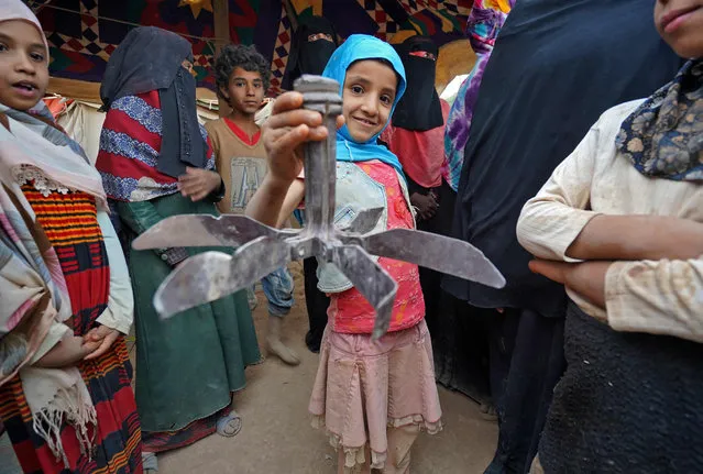 A girl holds propeller debris as she stands near other women and children by tents at the Suweida camp for people internally displaced by conflict, near Yemen's northern city of Marib, on April 15, 2021. The outcome of the scorched-earth battles raging around Marib city, the Saudi-backed Yemeni government's last northern stronghold, could significantly alter the future course of Yemen's conflict, now in its seventh year. The loss of Marib, gripped by a worsening humanitarian crisis, would be a heavy blow to the government, giving the Iran-aligned rebels more leverage in any future negotiations or even spur them to push further south, observers say. (Photo by Nabil Alawzari/AFP Photo)