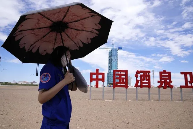 A worker holds an umbrella near the Shenzhou-12 spacecraft covered on the launch pad with the Chinese characters reading “China Jiuquan Satellite Launch Center” near Jiuquan on Wednesday, June 16, 2021. (Photo by Ng Han Guan/AP Photo)