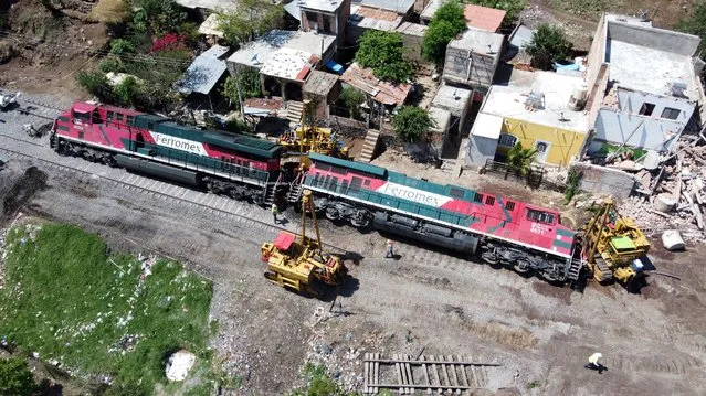 A picture made with a drone shows workers carry out the removal of a freight train that derailed, in the town of San Isidro Mazatepec, municipality of Tala, Jalisco state, Mexico, 16 June 2021. One person died and at least two others were injured when the train derailed and tumbled onto several houses adjacent to the railroad tracks. (Photo by Francisco Guasco/EPA/EFE)