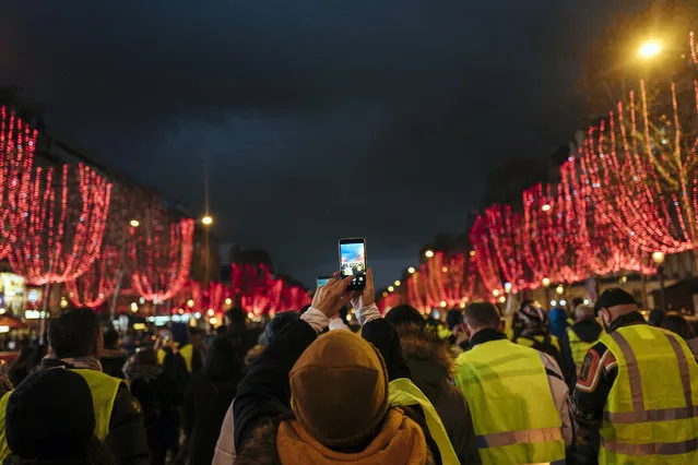 A demonstrator wears a yellow vest as she takes a photo on the Champs Elysees avenue in Paris, Saturday, December 22, 2018. France's yellow vest protesters, who have brought chaos to Paris over the past few weeks with their economic demands, demonstrated in sharply reduced numbers Saturday at the start of the Christmas and New Year holidays. (Photo by Kamil Zihnioglu/AP Photo)