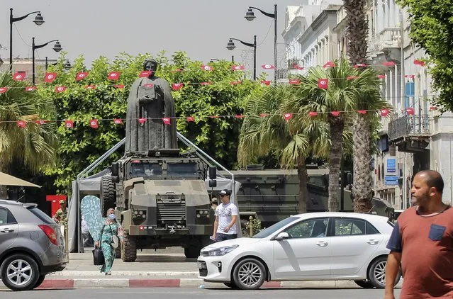 Tunisians walk past a military armored personnel carrier at Habib Bourguiba avenue in Tunis, Tunisia, Friday, July 30, 2021. Days of political turmoil in Tunisia over the economy and the coronavirus have left its allies in the Middle East, Europe and the United States watching to see if the fragile democracy will survive. (Photo by Hassene Dridi/AP Photo)