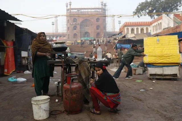 An Indian girl helps her mother with morning chores before they start their street food business on a cold winter morning in New Delhi, India, Thursday, December 29, 2016. Just as it is known for its scorching summers Delhi is known for its chilly winters. (Photo by Tsering Topgyal/AP Photo)