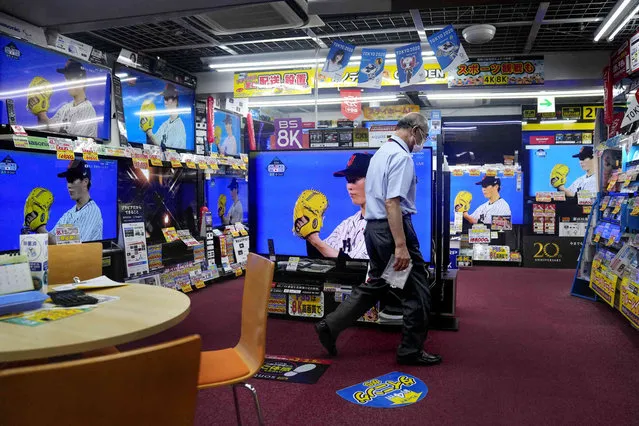 A salesman walks through an empty electronics store showroom as televisions broadcast the gold medal baseball game between Japan and the United States at the 2020 Summer Olympics, Saturday, August 7, 2021, in Tokyo. (Photo by AP Photo)
