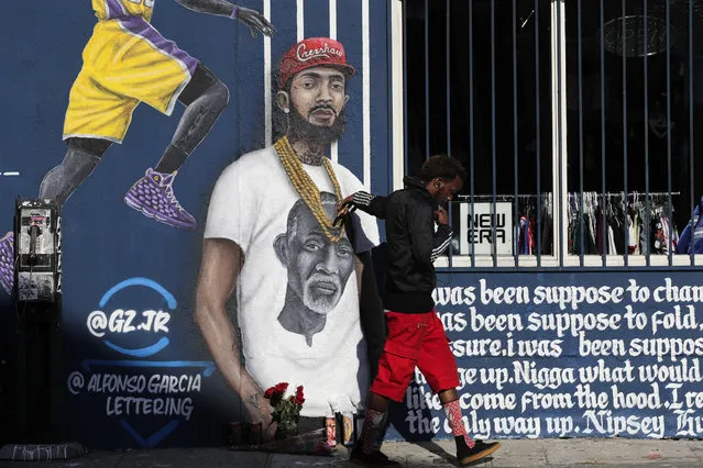 A man touches a mural depicting slain rapper Nipsey Hussle, Tuesday, April 2, 2019, in Los Angeles. Hussle was shot and killed Sunday, March 31, outside of his clothing store in Los Angeles. (Photo by Jae C. Hong/AP Photo)