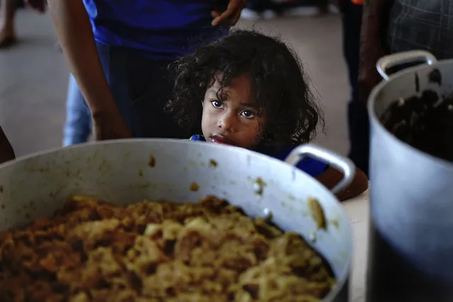 A child, who is with a migrant caravan that is slowly moving north, waits for a meal at the “Casa del Peregrino” San Juan Diego shelter in Mexico City, Monday, December 13, 2021. (Photo by Marco Ugarte/AP Photo)