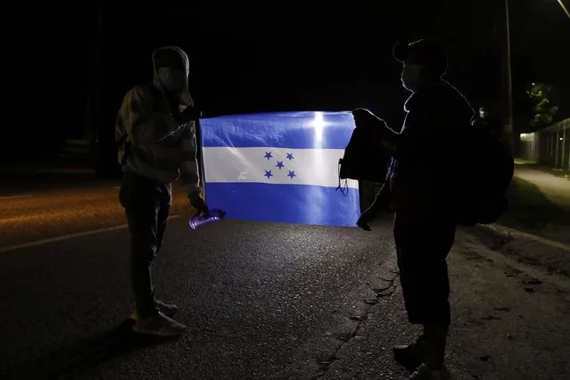 Members of a migrant caravan hold a Honduran national flag as they begin their journey in the hopes of reaching the United States, in San Pedro Sula, Honduras, Saturday, January 15, 2022. (Photo by Delmer Martinez/AP Photo)