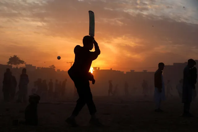 A boy is silhouetted against the setting sun as he plays cricket on New Year's Eve, in Peshawar, Pakistan on December 31, 2021. (Photo by Fayaz Aziz/Reuters)