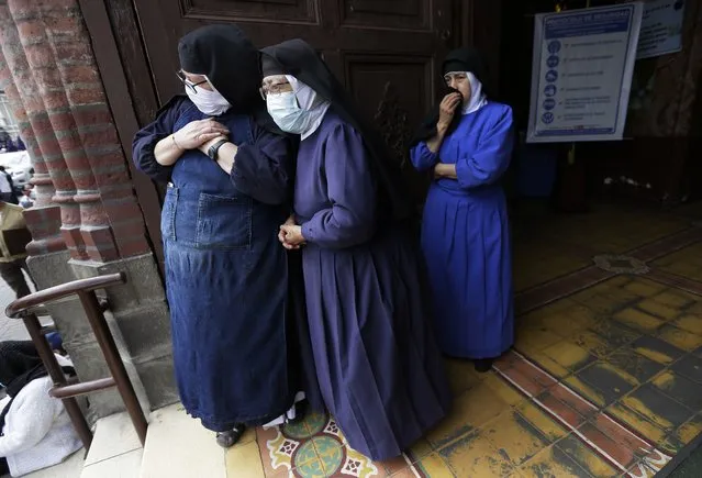 Nuns watch from the doorway of a church as the statue of the Lord of Good Success leads the Holy Week procession in Riobamba, Ecuador, Tuesday, March 30, 2021. Due to the COVID-19 pandemic, the sacred image did not have the crowds that usually accompany it in the procession. (Photo by Dolores Ochoa/AP Photo)