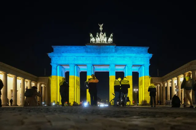 People look at the Brandenburg Gate after it was illuminated in the colours of the Ukrainian flag to show solidarity with the country during the tensions with Russia in Berlin, Germany, Wednesday, February 23, 2022. (Photo by Markus Schreiber/AP Photo)
