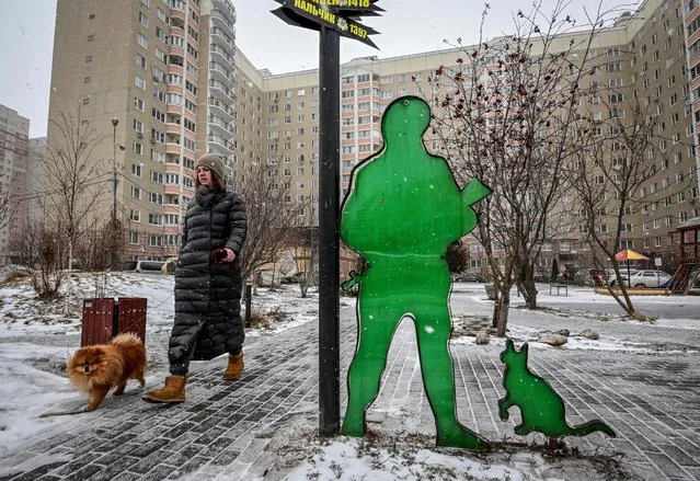 A woman walks a dog past the so-called “people's installation to a Russian soldier” nicknamed the “polite people” created by residents in the backyard of their apartment building in the town of Podolsk, outside Moscow, on March 28, 2022. (Photo by Yuri Kadobnov/AFP Photo)