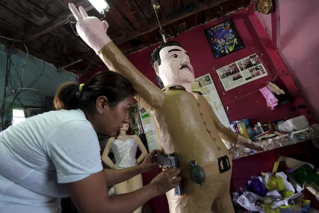 A worker attaches a toy gun and toy grenade onto a pinata depicting the drug lord Joaquin “El Chapo” Guzman at a workshop in Reynosa, July 21, 2015. (Photo by Daniel Becerril/Reuters)