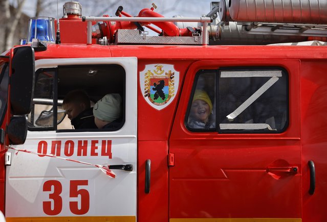 Children sit in a fire truck with letter Z, which has become a symbol of the Russian military, stuck on a window, during a city holiday in the city of Olonets, 300 km (186 miles) north-east of St. Petersburg, Russia, Sunday, May 1, 2022. (Photo by AP Photo/Stringer)