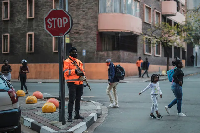 Pedestrians cross a street as a private security guard stands with a semi-automatic rifle loaded with rubber bullets in Hillbrow, Johannesburg, on April 17, 2020. (Photo by Marco Longari/AFP Photo)