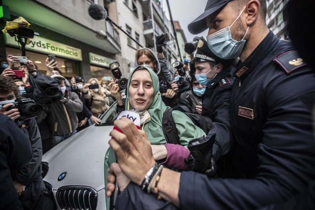 Silvia Romano, escorted by Carabinieri, lowers her face mask for press as she arrives at her home, in Milan, Italy, Monday, May 11, 2020. The young Italian woman has returned to her homeland after 18 months as a hostage in eastern Africa. (Photo by Luca Bruno/AP Photo)