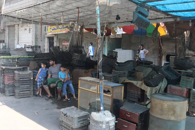 Civilians sit amid empty empty plastic crates at a closed shop in Aleppo's rebel-controlled al-Shaar neighbourhood due to a siege by Syrian pro-government forces that cut the supply lines into opposition-held areas of the city, Syria August 5, 2016. (Photo by Abdalrhman Ismail/Reuters)