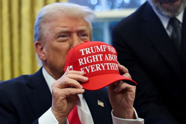 U.S. President Donald Trump holds a hat after signing an executive order in the Oval Office, at the White House on February 25, 2025. (Photo by Evelyn Hockstein/Reuters)