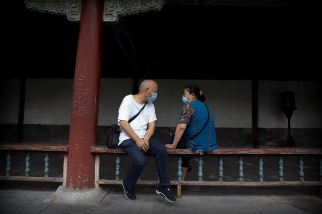 People wearing face masks to protect against the coronavirus sit on a railing at the Temple of Heaven in Beijing, Saturday, July 18, 2020. Authorities in a city in far western China have reduced subways, buses and taxis and closed off some residential communities amid a new coronavirus outbreak, according to Chinese media reports. They also placed restrictions on people leaving the city, including a suspension of subway service to the airport. (Photo by Mark Schiefelbein/AP Photo)