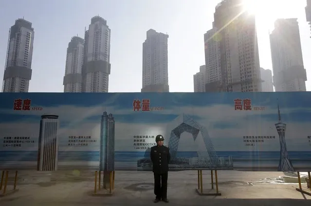 A security guard stands next to an advertising board in front of a residential compound under construction in Wuhan, Hubei province in this January 21, 2014 file photo. China's policymakers think they can stem a rapid rundown of their foreign exchange reserves and ease pressure on the currency by pump-priming the economy to meet this year's growth target, sources involved in policy discussions said. (Photo by Reuters/Stringer)